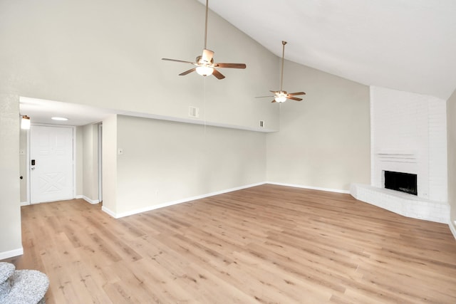 unfurnished living room with ceiling fan, high vaulted ceiling, a fireplace, and light hardwood / wood-style flooring