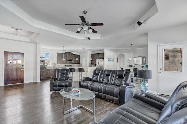 living room with a tray ceiling, ceiling fan, and dark wood-type flooring