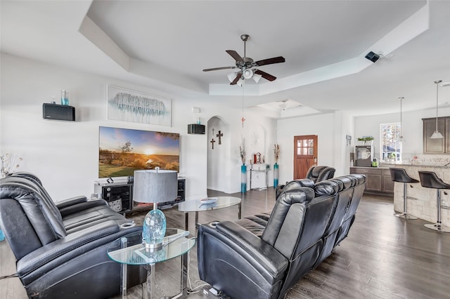 living room with a tray ceiling, ceiling fan, and dark wood-type flooring