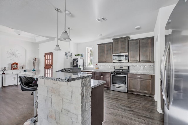 kitchen featuring appliances with stainless steel finishes, dark hardwood / wood-style flooring, light stone counters, and hanging light fixtures