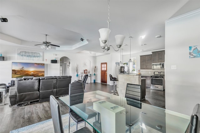 dining area featuring ceiling fan with notable chandelier, dark hardwood / wood-style flooring, and a tray ceiling