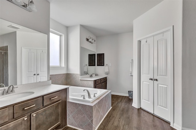 bathroom featuring wood-type flooring, vanity, and tiled tub