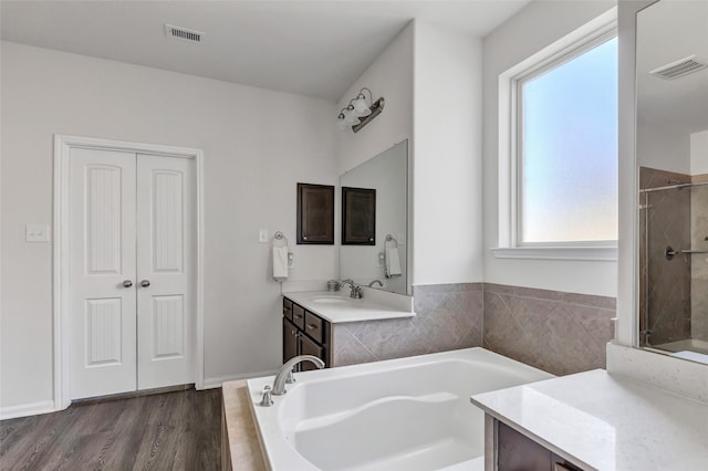 bathroom with hardwood / wood-style floors, plenty of natural light, plus walk in shower, and vanity