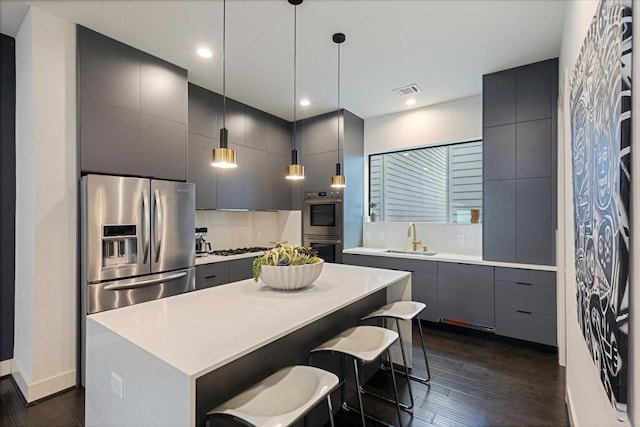 kitchen featuring sink, a center island, dark wood-type flooring, pendant lighting, and appliances with stainless steel finishes