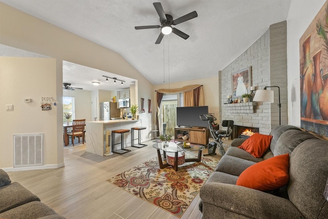 living room featuring a brick fireplace, a textured ceiling, light hardwood / wood-style flooring, and a healthy amount of sunlight