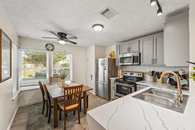 kitchen with sink, gray cabinets, light wood-type flooring, a textured ceiling, and appliances with stainless steel finishes