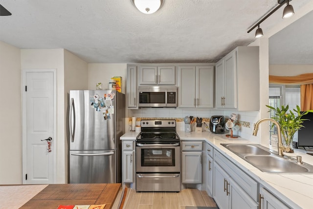 kitchen featuring appliances with stainless steel finishes, a textured ceiling, sink, light hardwood / wood-style flooring, and gray cabinets