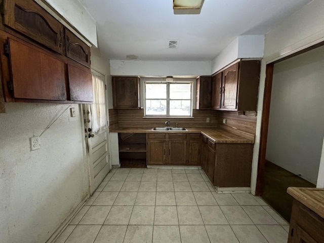 kitchen with decorative backsplash, light tile patterned flooring, dark brown cabinetry, and sink