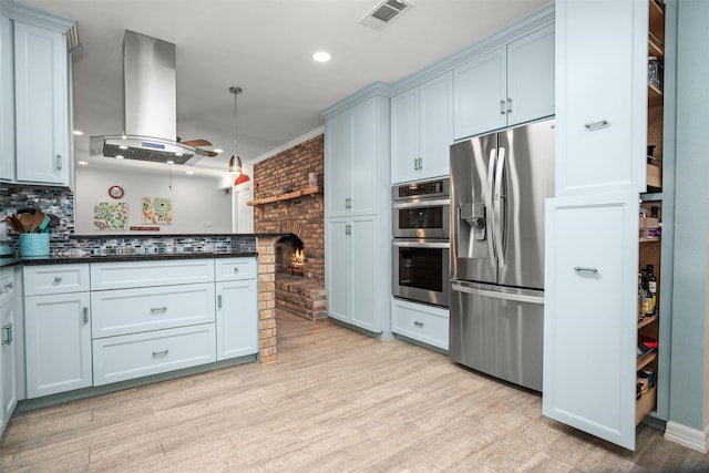 kitchen featuring light wood-type flooring, island range hood, a fireplace, appliances with stainless steel finishes, and ornamental molding