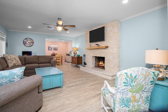 living room featuring ceiling fan, a stone fireplace, crown molding, and light hardwood / wood-style flooring