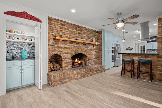 living room featuring ceiling fan, light hardwood / wood-style floors, ornamental molding, and a brick fireplace