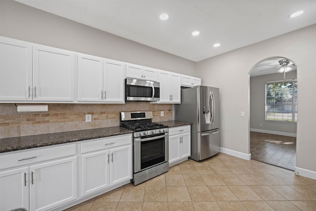 kitchen featuring dark stone countertops, white cabinets, backsplash, light tile patterned floors, and stainless steel appliances