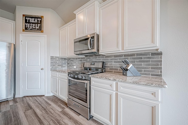 kitchen featuring appliances with stainless steel finishes, light stone countertops, white cabinets, vaulted ceiling, and light wood-type flooring