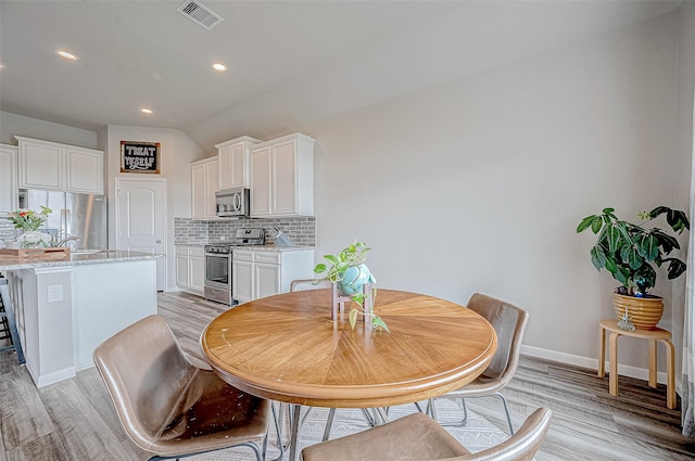 dining space with vaulted ceiling and light hardwood / wood-style flooring