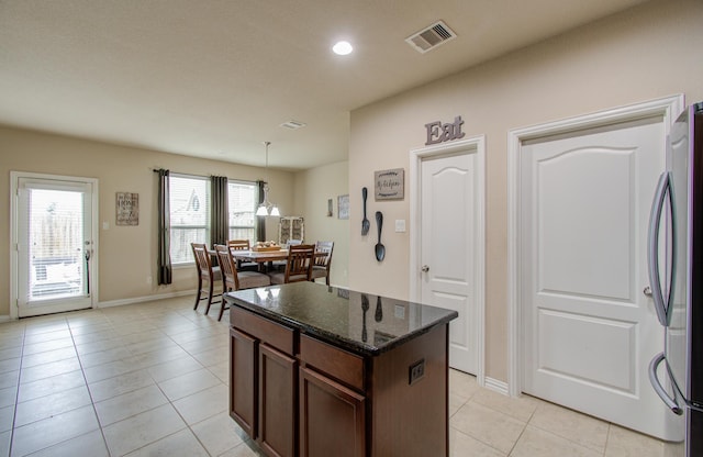 kitchen with stainless steel refrigerator, dark stone countertops, light tile patterned floors, and a kitchen island