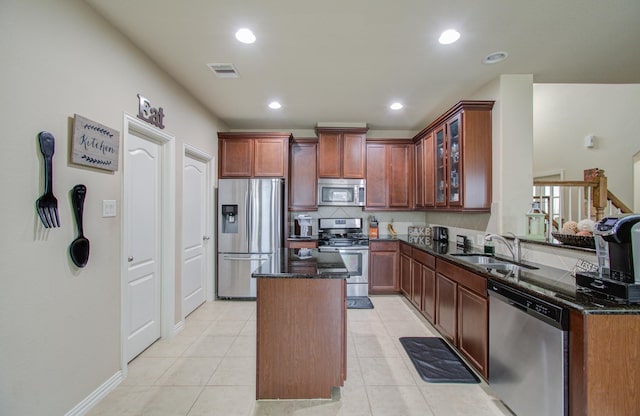 kitchen featuring dark stone counters, sink, light tile patterned floors, appliances with stainless steel finishes, and kitchen peninsula