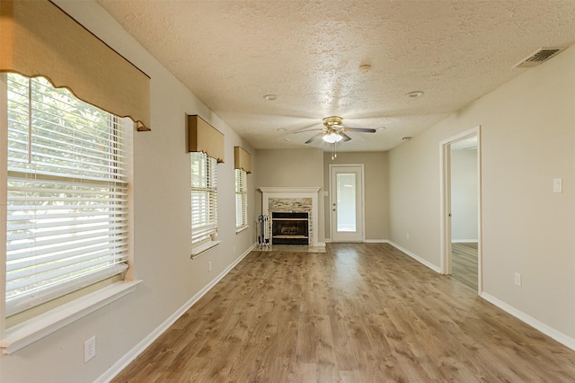 unfurnished living room featuring a fireplace, a textured ceiling, light wood-type flooring, and ceiling fan