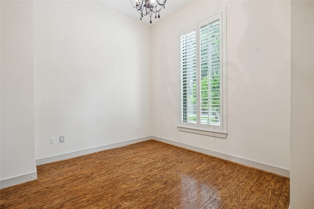 empty room with wood-type flooring and an inviting chandelier