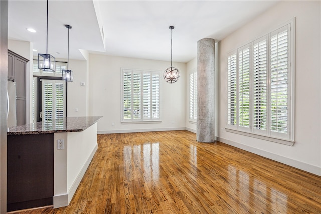 kitchen featuring light wood-type flooring, hanging light fixtures, a healthy amount of sunlight, and dark stone countertops