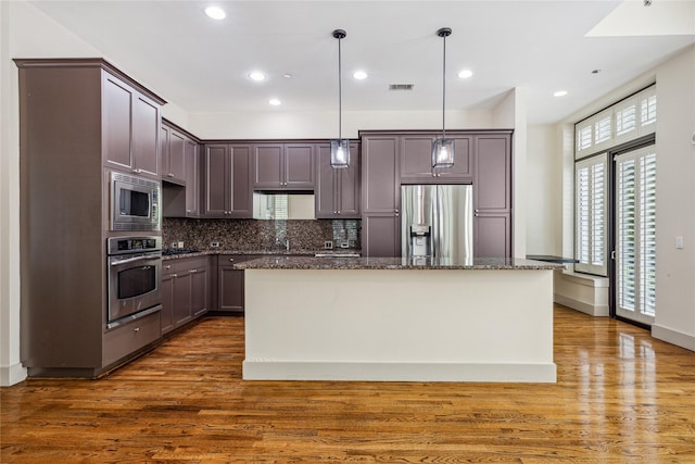 kitchen featuring dark hardwood / wood-style flooring, dark stone counters, stainless steel appliances, decorative light fixtures, and a center island