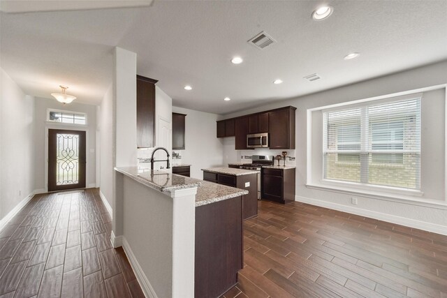 kitchen featuring light stone countertops, appliances with stainless steel finishes, dark hardwood / wood-style flooring, and kitchen peninsula