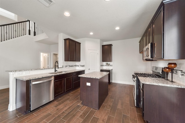 kitchen featuring sink, dark hardwood / wood-style floors, kitchen peninsula, a kitchen island, and appliances with stainless steel finishes