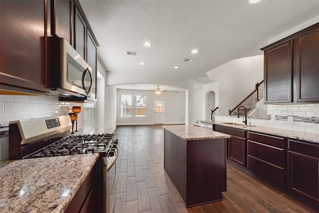 kitchen with light stone countertops, sink, stainless steel appliances, dark hardwood / wood-style floors, and a kitchen island