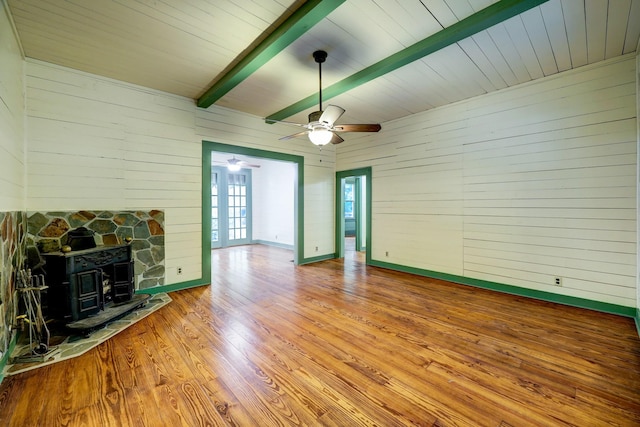 unfurnished living room featuring french doors, light wood-type flooring, ceiling fan, beamed ceiling, and a wood stove