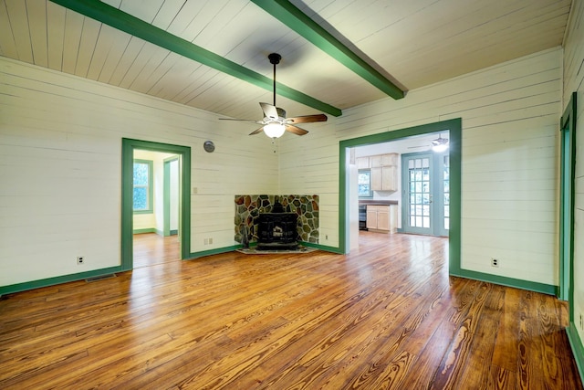 unfurnished living room with beamed ceiling, hardwood / wood-style floors, a wood stove, and a wealth of natural light