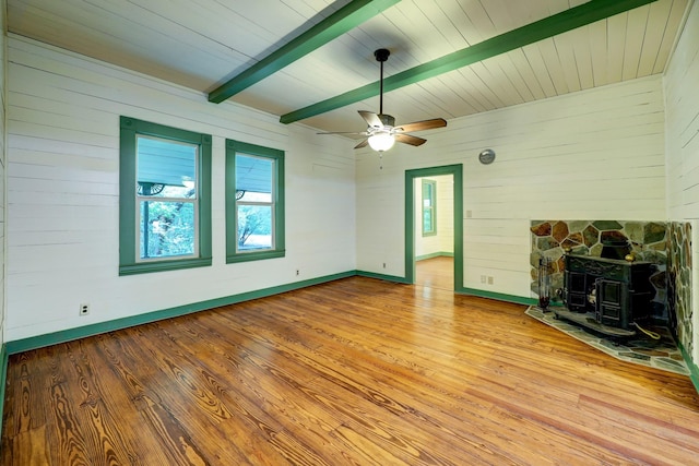 unfurnished living room with beamed ceiling, light wood-type flooring, a wood stove, and ceiling fan