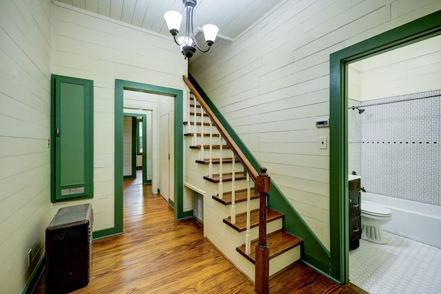 stairs featuring wood-type flooring, an inviting chandelier, and wooden walls