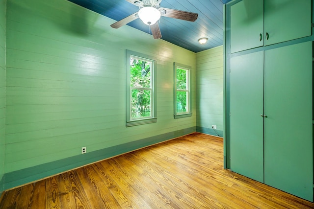 unfurnished bedroom with a closet, light hardwood / wood-style floors, ceiling fan, and wooden walls