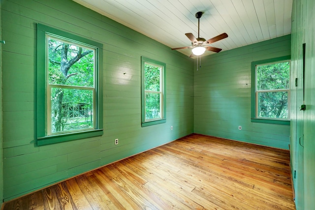 empty room featuring ceiling fan, light wood-type flooring, and wooden walls