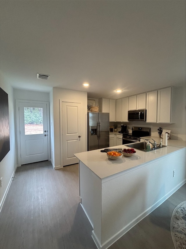 kitchen with light hardwood / wood-style floors, kitchen peninsula, sink, appliances with stainless steel finishes, and white cabinets