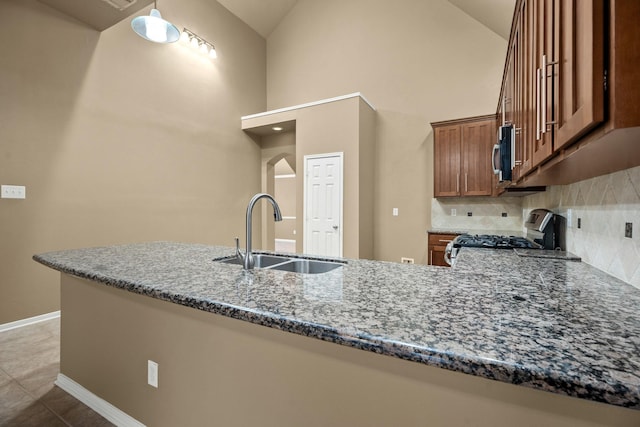 kitchen featuring dark stone counters, sink, decorative backsplash, kitchen peninsula, and stainless steel appliances