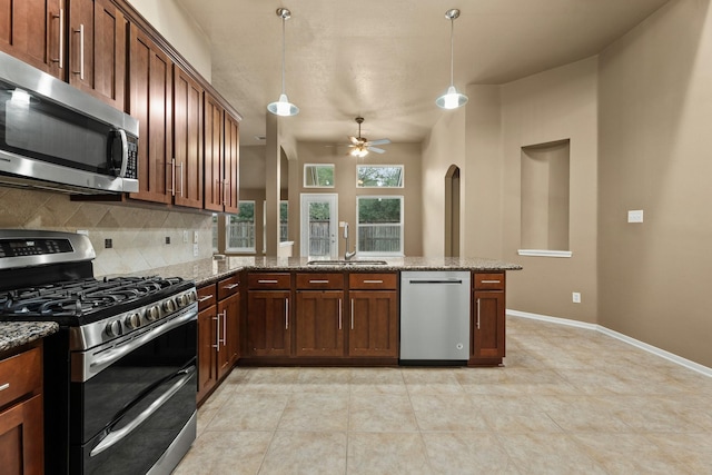 kitchen featuring stone counters, sink, kitchen peninsula, decorative light fixtures, and appliances with stainless steel finishes