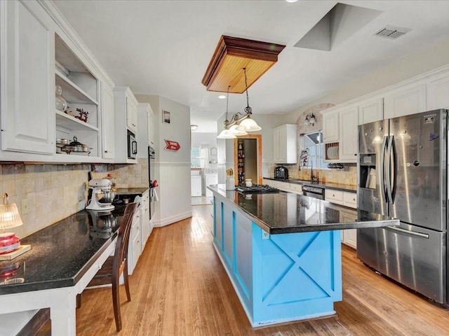 kitchen featuring stainless steel appliances, light hardwood / wood-style floors, white cabinetry, hanging light fixtures, and a breakfast bar area