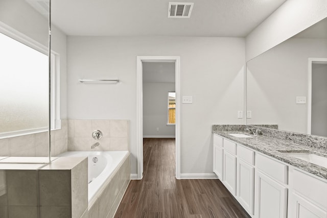 bathroom with hardwood / wood-style floors, a relaxing tiled tub, and vanity