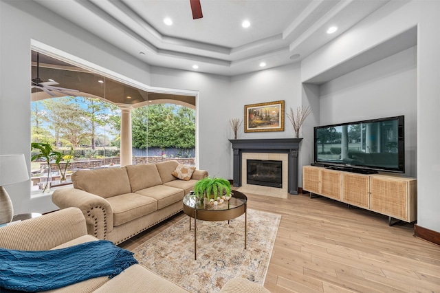 living room with a tray ceiling, a fireplace, and light hardwood / wood-style floors