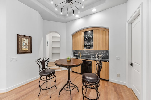 dining room with light hardwood / wood-style floors, a raised ceiling, and bar