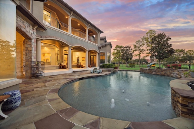 pool at dusk featuring a patio area and pool water feature