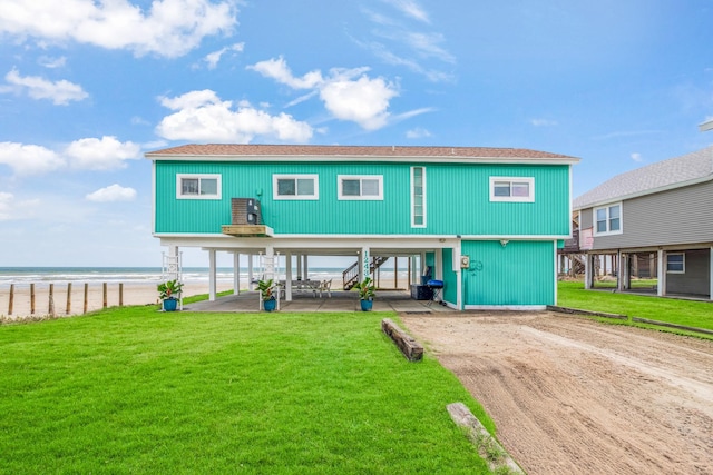 back of property with a water view, a carport, a yard, and a view of the beach