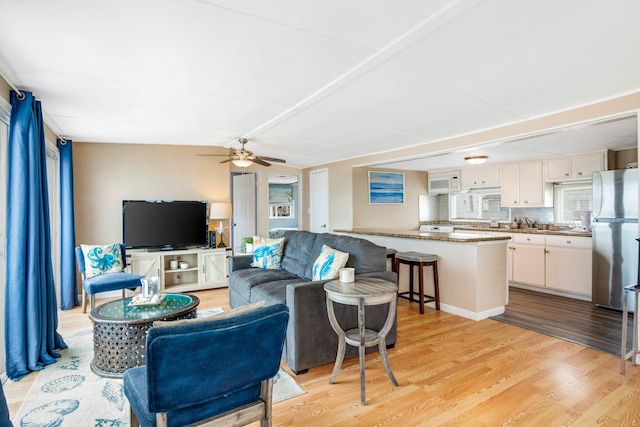 living room with ceiling fan, sink, vaulted ceiling, and light hardwood / wood-style flooring