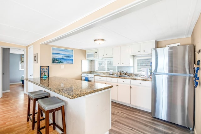 kitchen with stone countertops, a peninsula, white appliances, light wood-style floors, and white cabinets