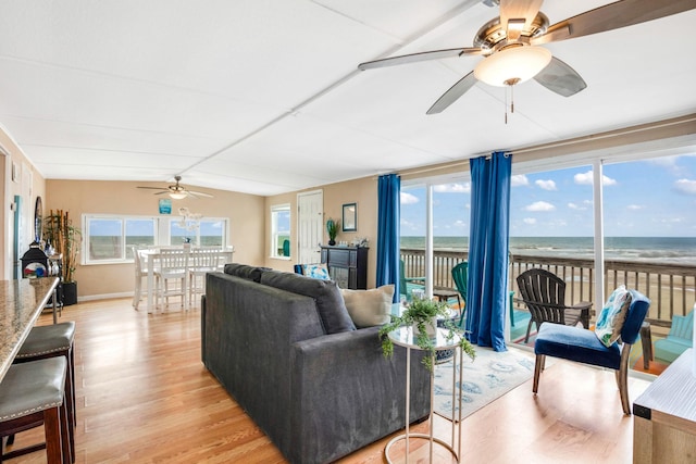 living room featuring a water view, light wood-type flooring, a view of the beach, and a wealth of natural light