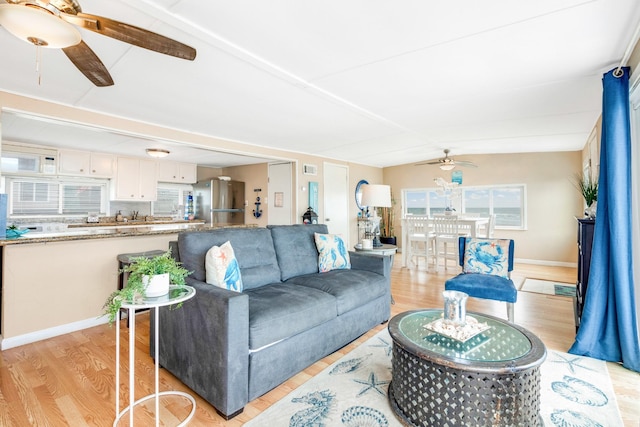 living room with ceiling fan, lofted ceiling, light wood-style flooring, and baseboards