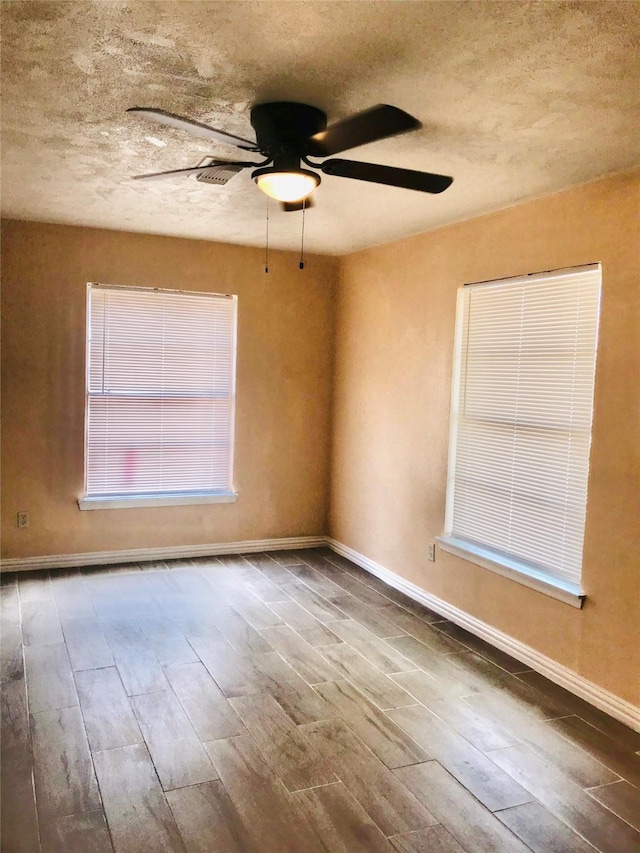 empty room featuring wood-type flooring, a textured ceiling, a wealth of natural light, and ceiling fan