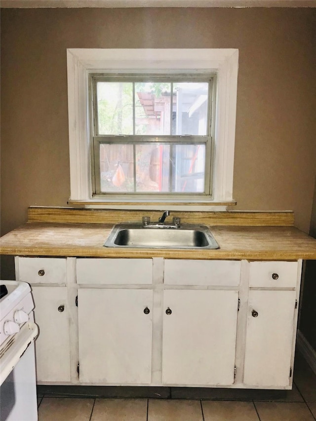 kitchen featuring white cabinets, light tile patterned floors, electric range, and sink