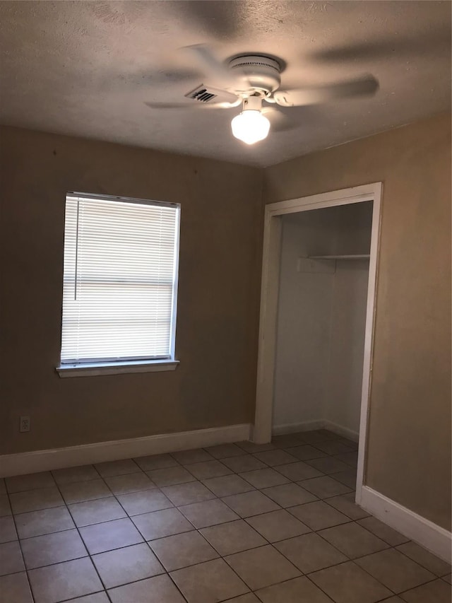 unfurnished bedroom featuring ceiling fan, a closet, light tile patterned floors, and a textured ceiling