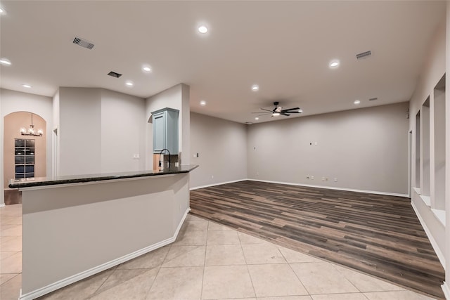 kitchen with kitchen peninsula, ceiling fan with notable chandelier, light hardwood / wood-style flooring, and dark stone countertops